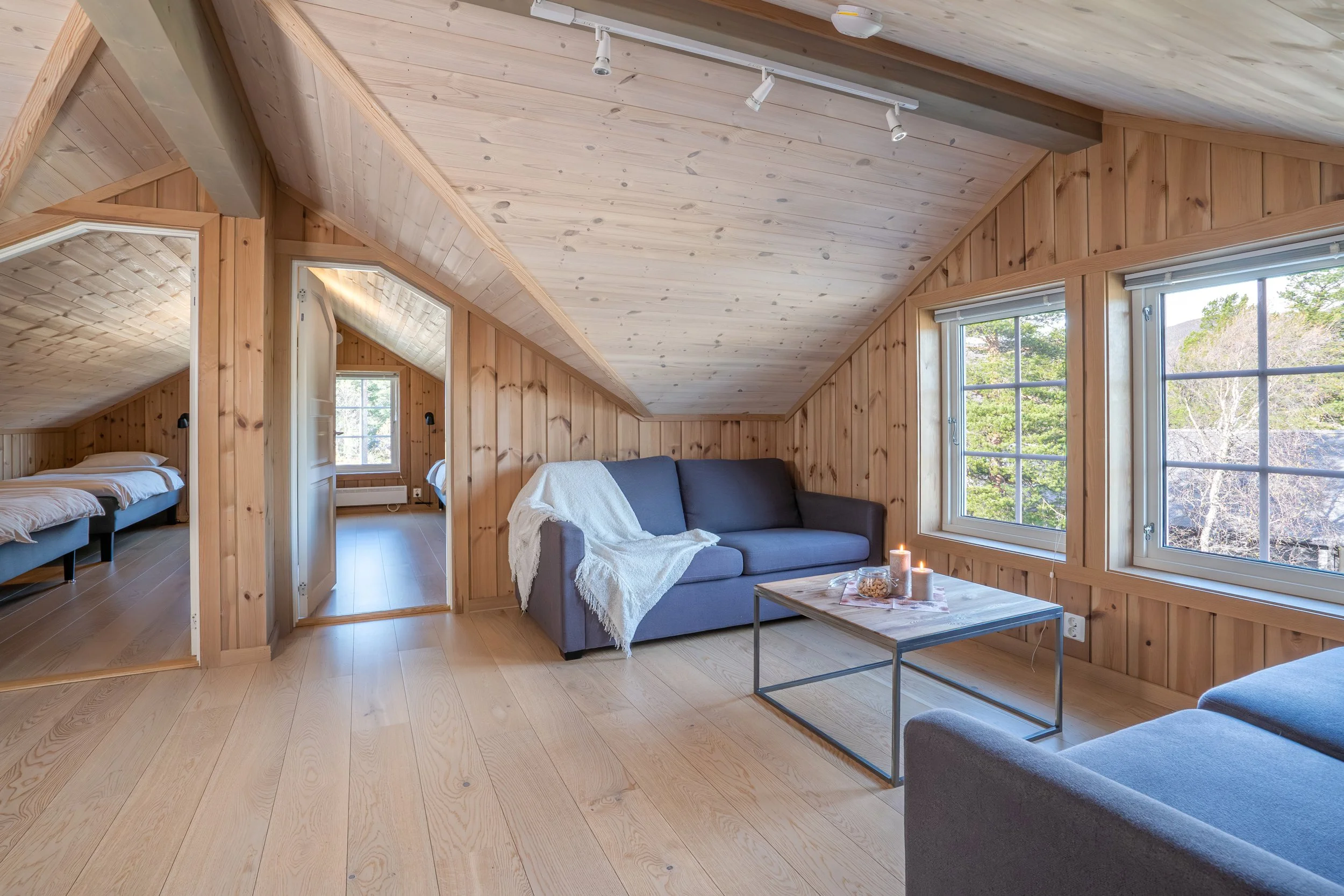 Loftstue med sofa og sofabord. Åpne dører inn til soverom. Foto