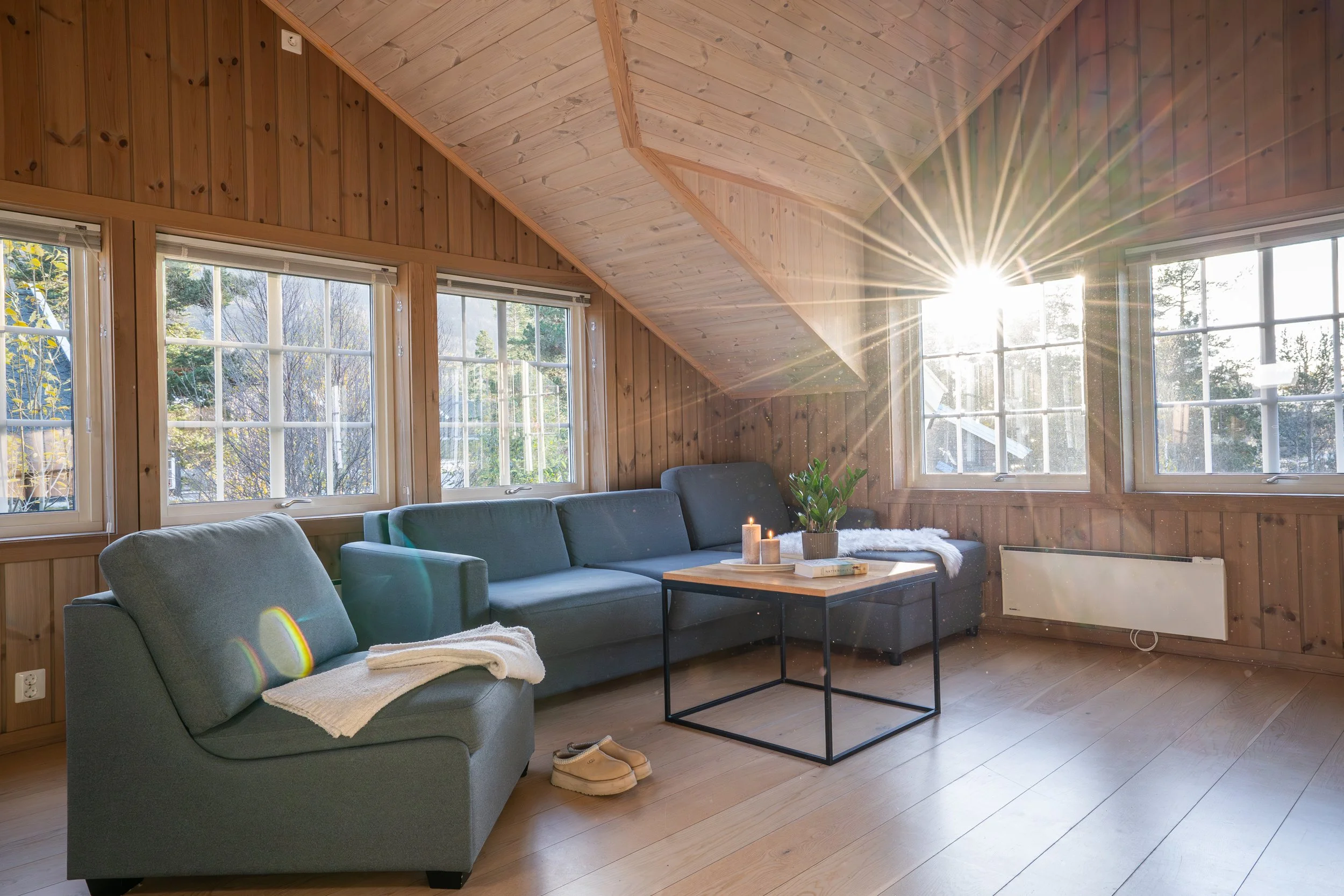 Loftstue med sofa og lenestol. Solen skinner inn gjennom vinduet. Foto