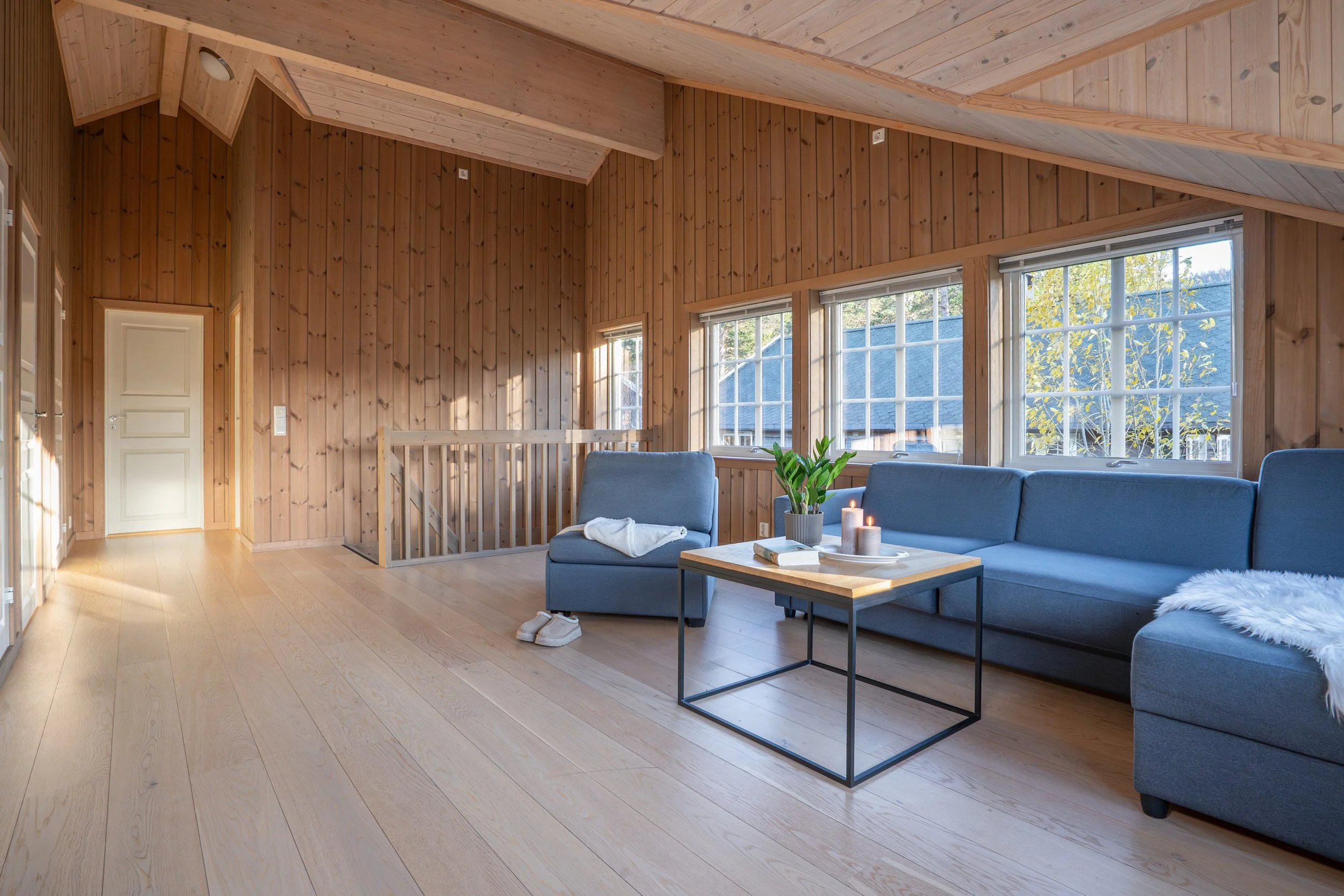 Stor loftstue med sofa og lenestol. Store vinduer og mye naturlig lys. Foto