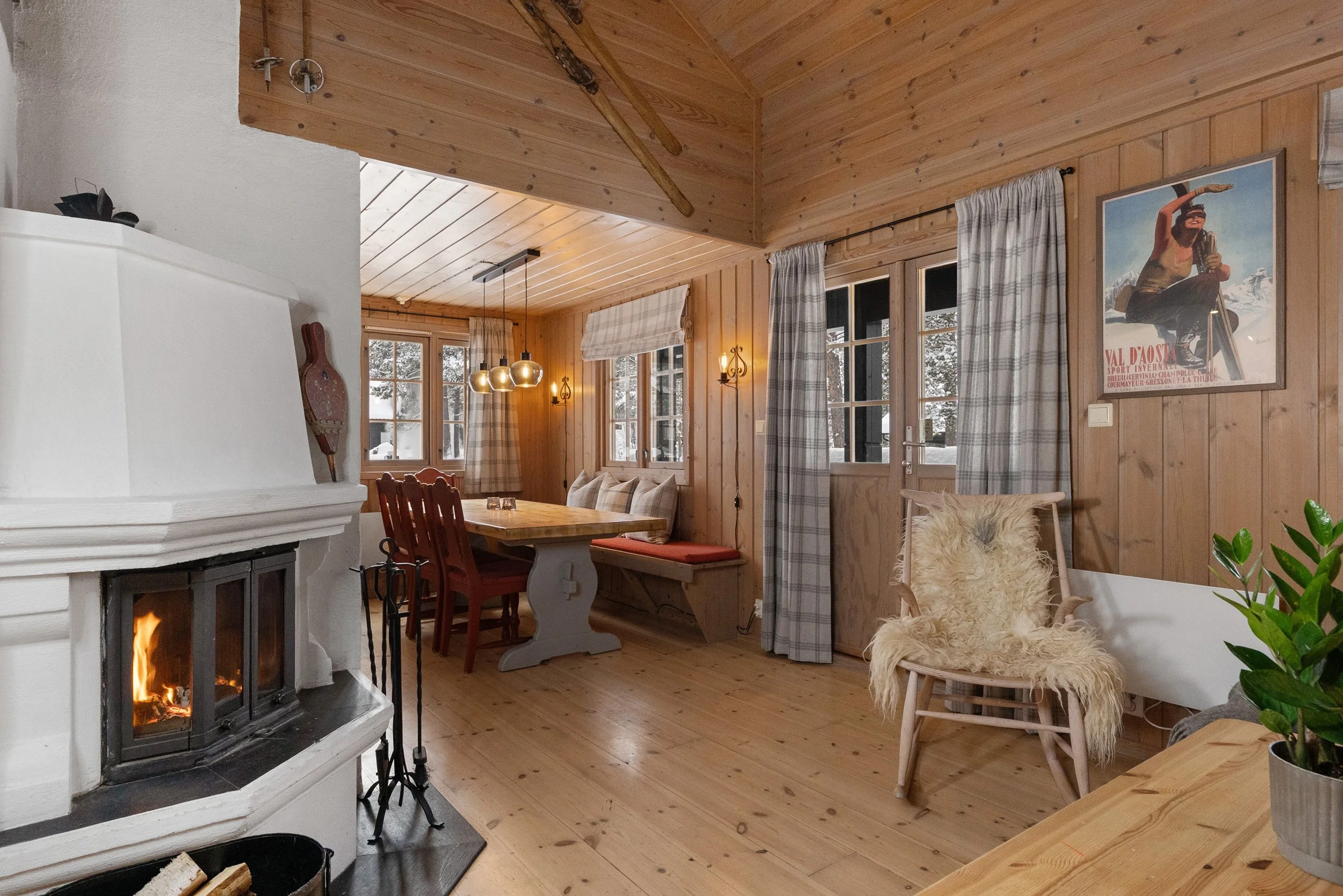 Cabin living room with fireplace and rocking chair. Open kitchen with dining table in the background. Photo
