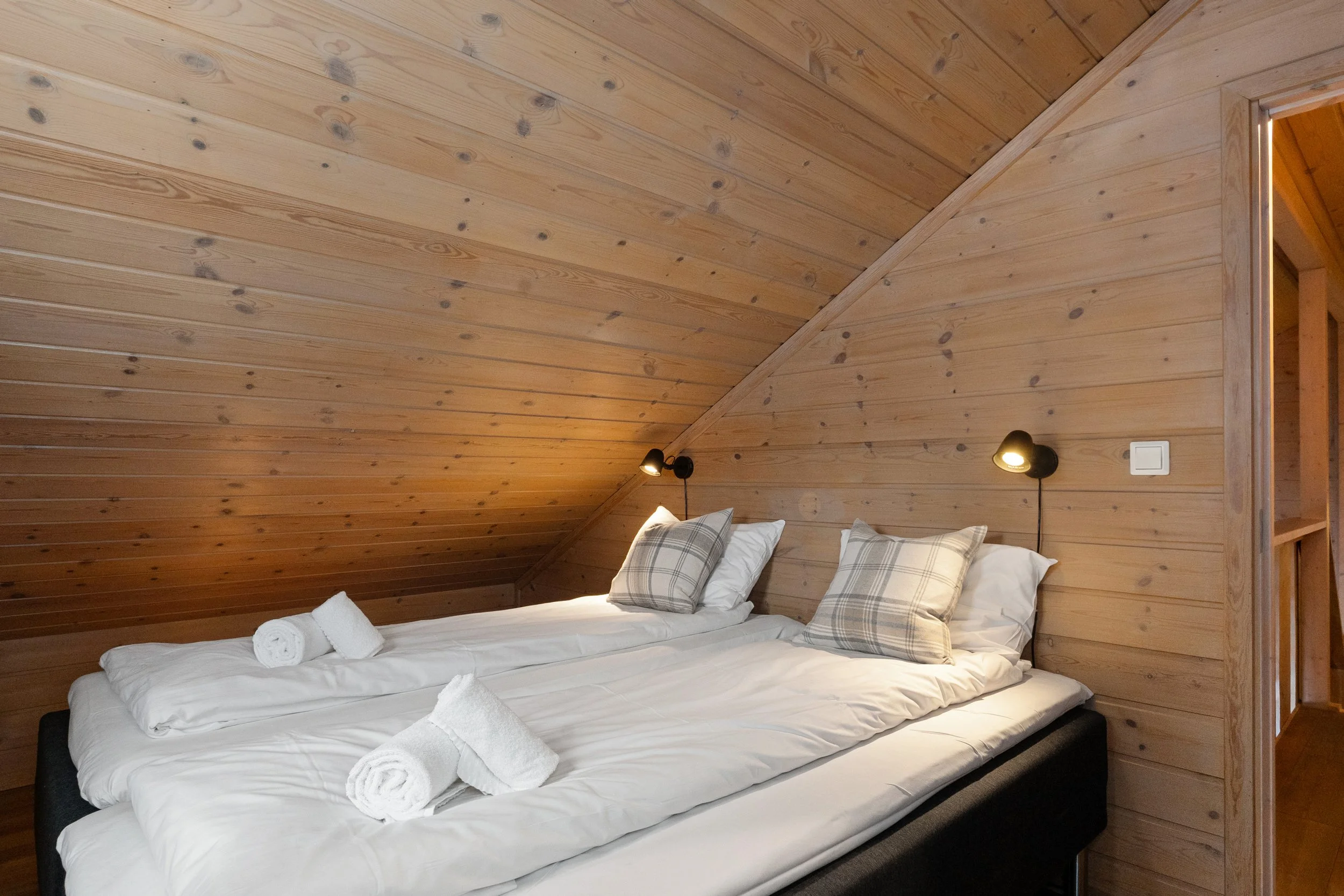 Bedroom with a made-up double bed. Towels are neatly rolled up on the bed. Photo