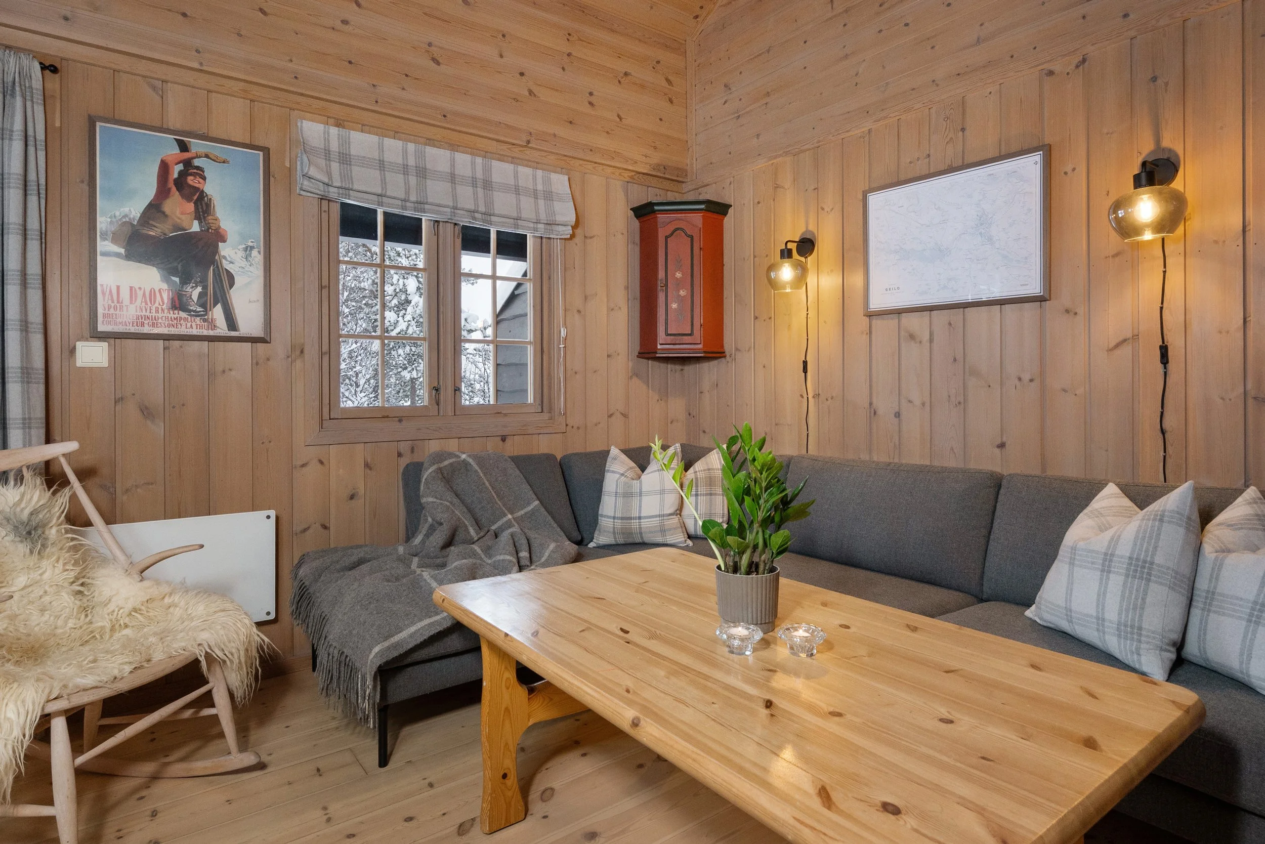 Sofakrok i hytte. Bordet er pyntet med plante og telys. En gyngestol med saueskinn står i hjørnet. Foto