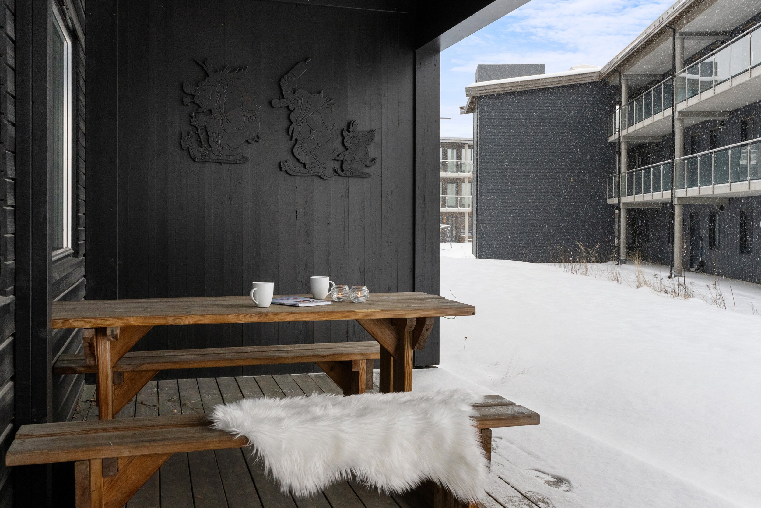 Terrasse i vinterlige omgivelser. Saueskinn ligger på benk, og kaffekopper står på bordet. Foto