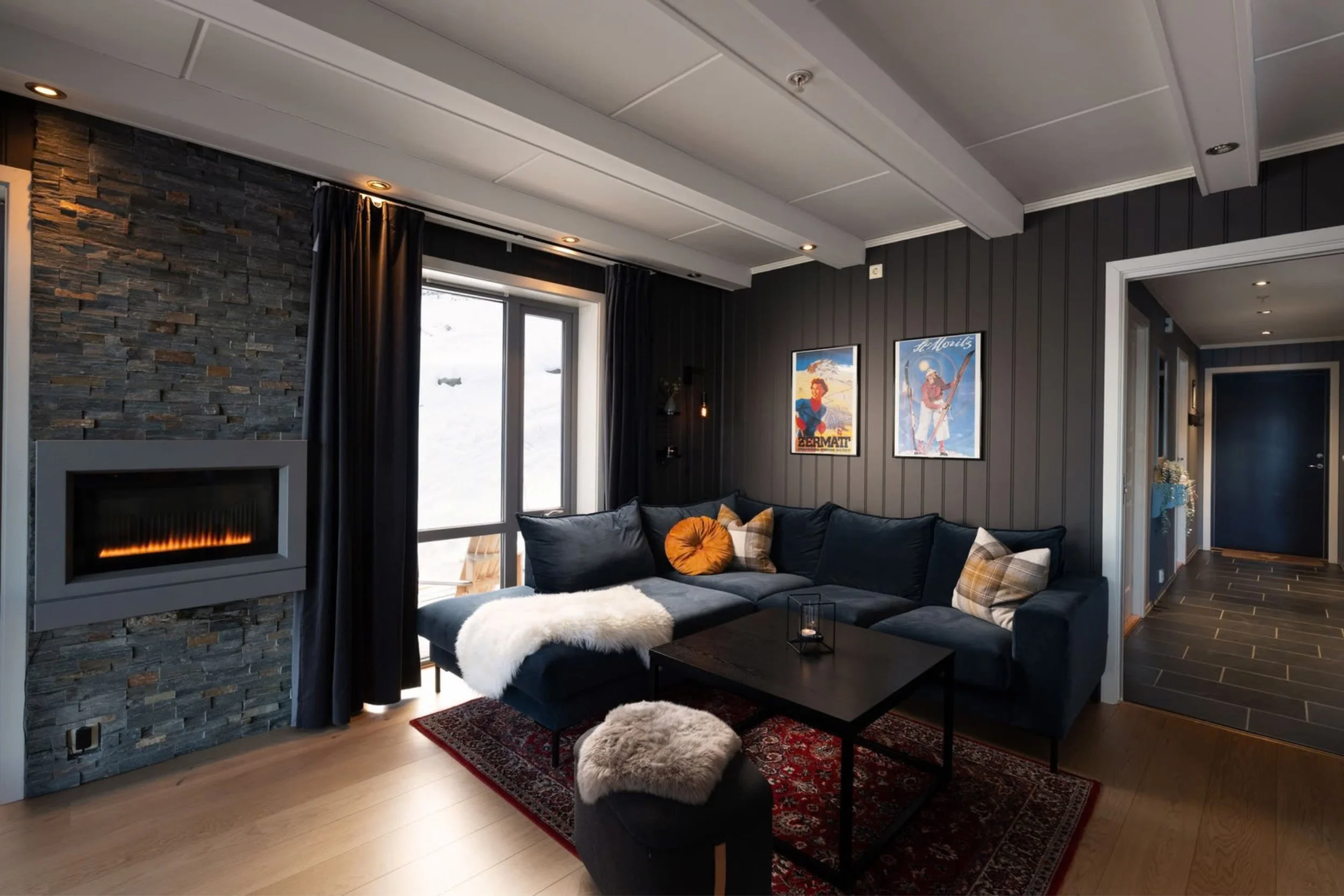 Åpen stue med vinduer fra gulv til tak. Peis, sofa og sofabord. Foto