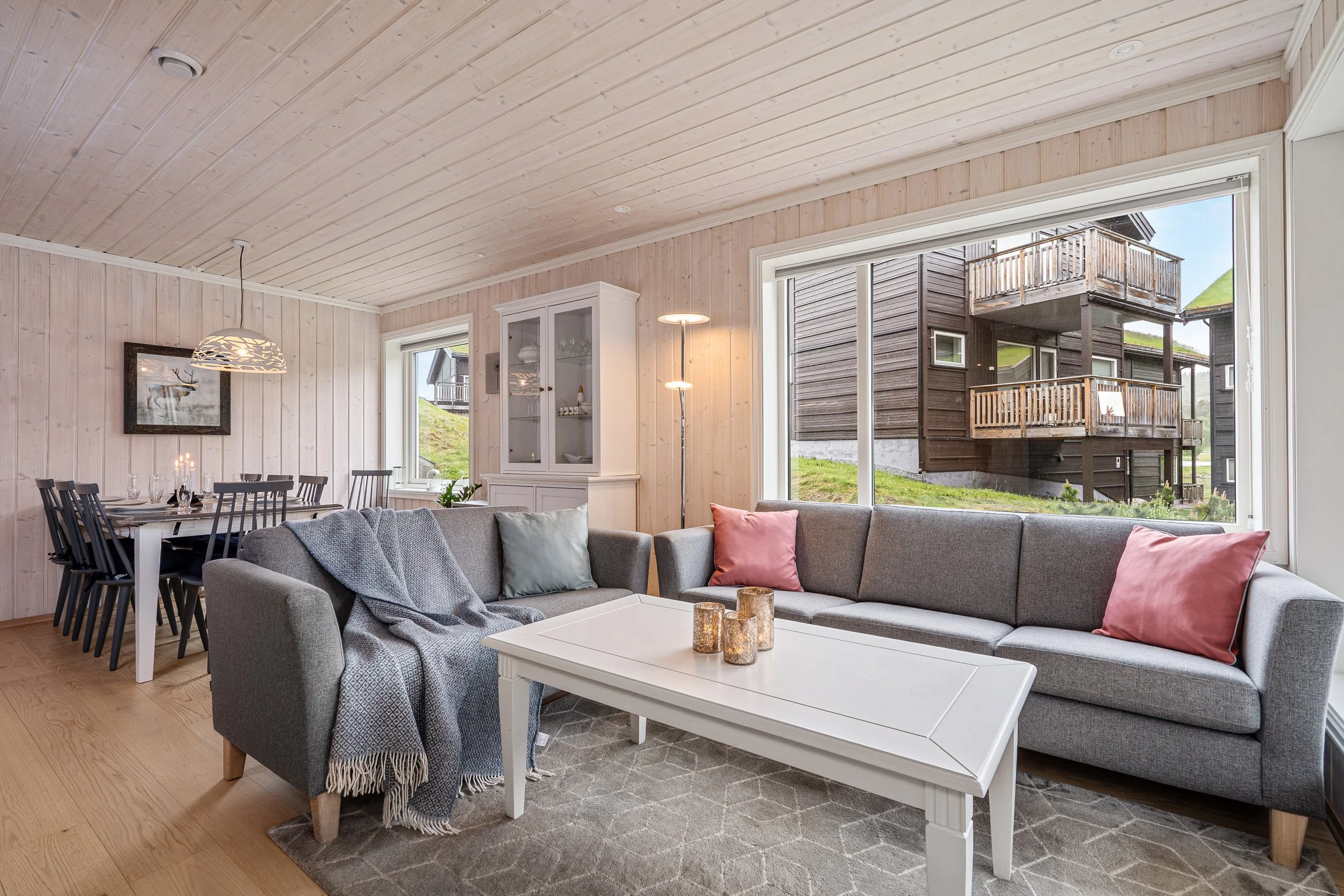 Bright living room with large windows. Dining room visible in the background. Photo