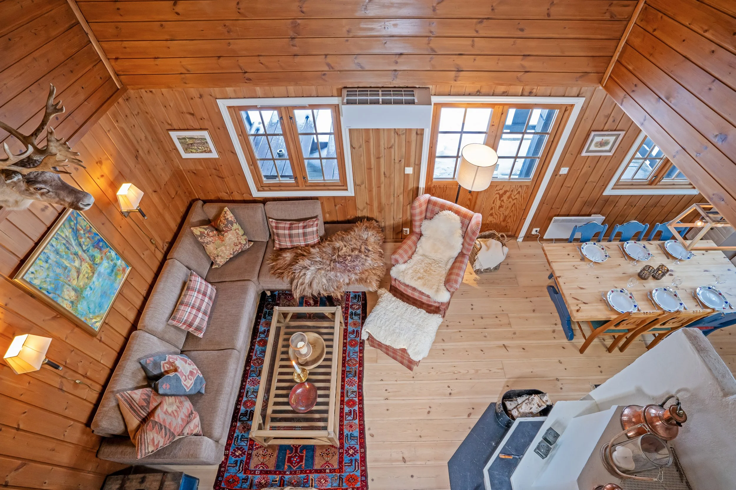 Cabin living room with sofa corner and dining table. Sheepskin and pillows on the sofa and chair. 