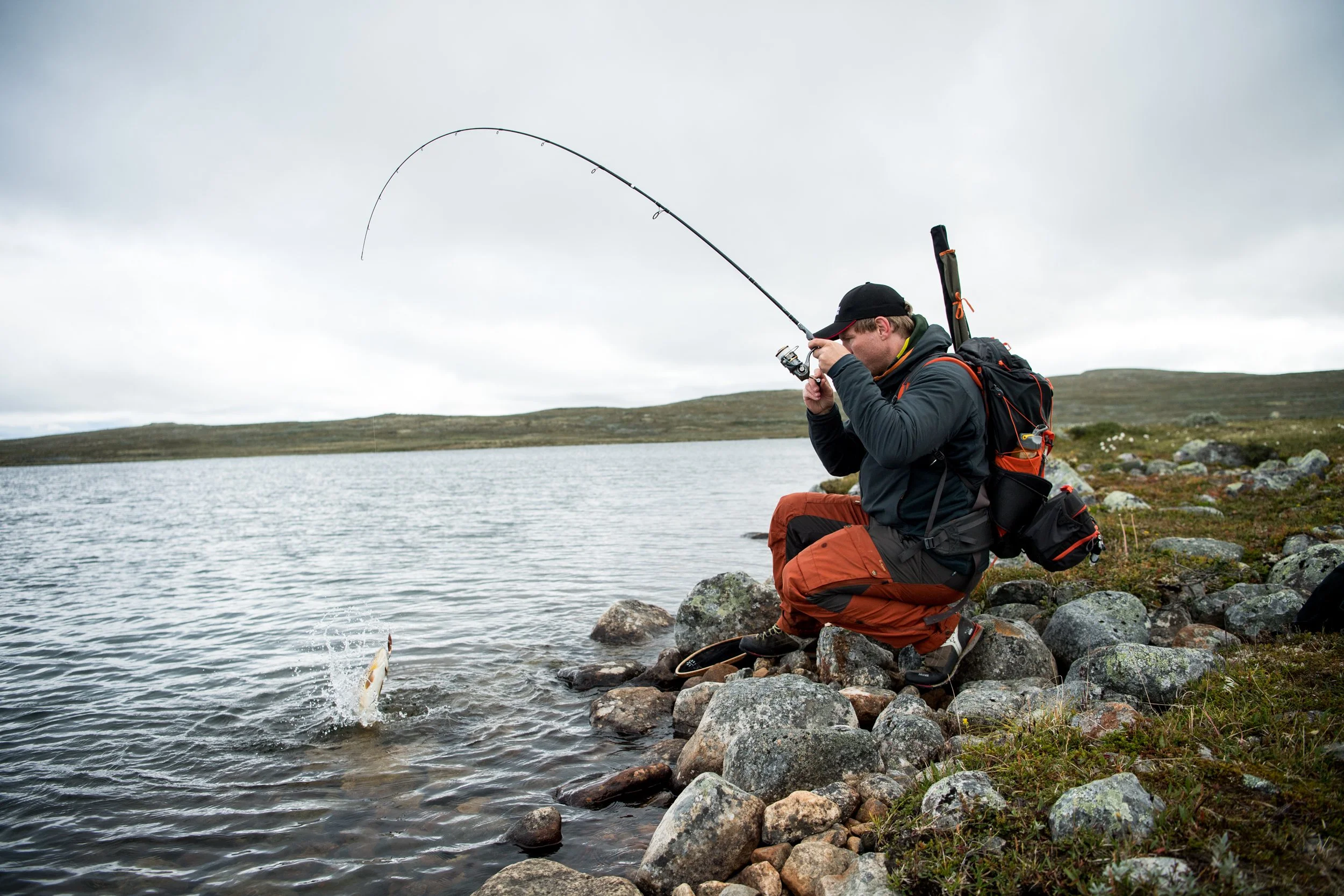 En mann snurrer inn fiskestang med fisk på kroken.
