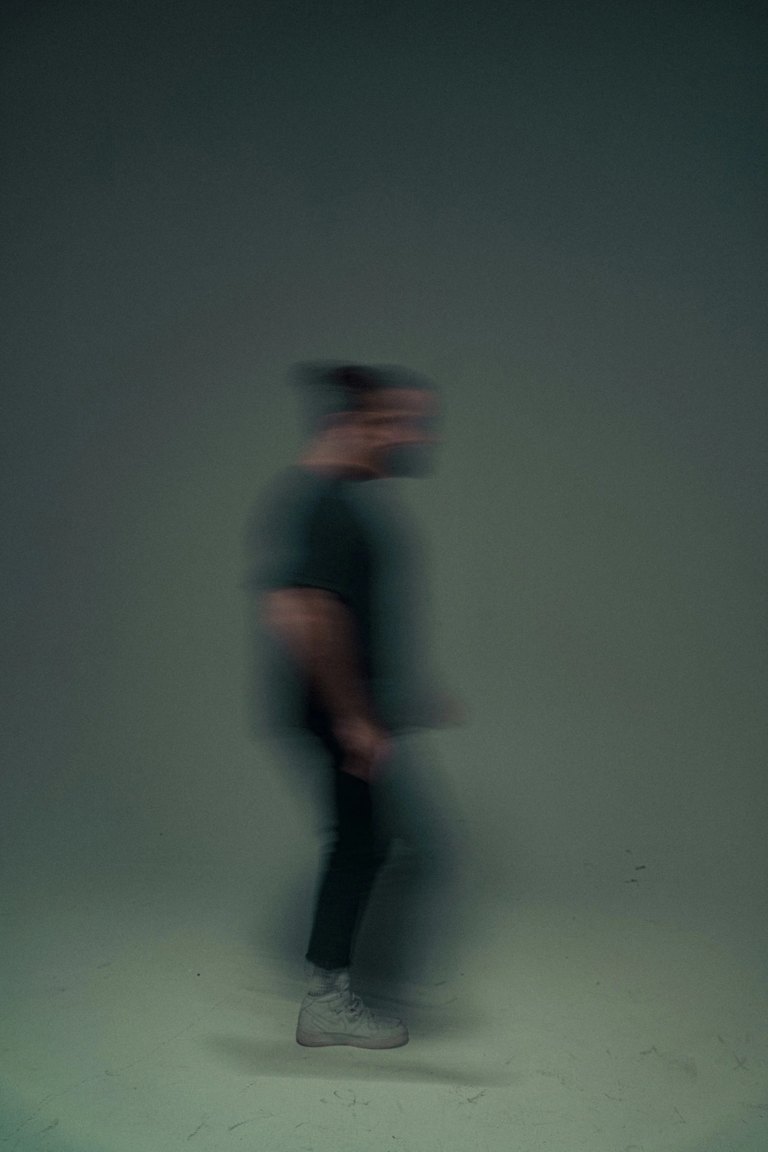 En person står mot en grå vägg, men är mycket suddig och oskarp, vilket gör att man inte kan se detaljer tydligt.
