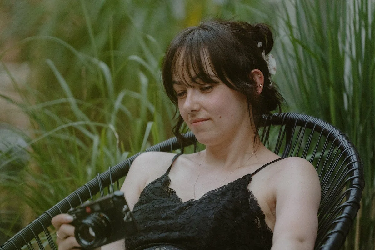 Hochzeitsfotografin für Destination Weddings schaut auf eine Kamera, während sie auf einem Stuhl auf Mallorca sitzt