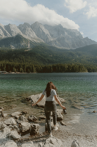 Hochzeitsfotografin spaziert mit einer Kamera in der Hand über Steine in einen See in Südtirol hinein