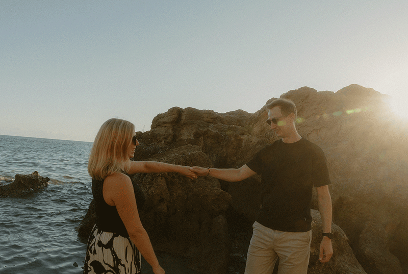 Ein Paar hält sich lächelnd an den Händen an der Felsküste auf Mallorca, eingefangen bei einem emotionalen Fotoshooting
