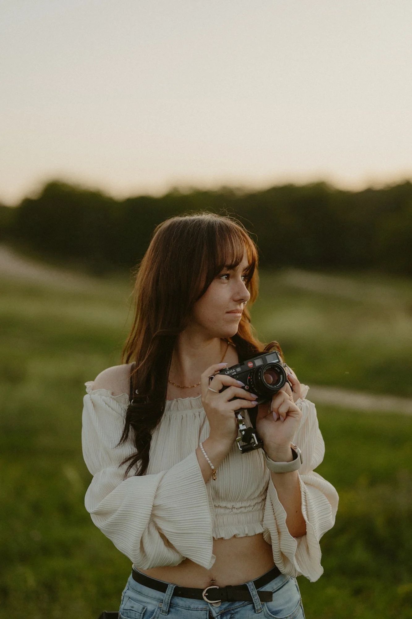 Portrait einer Hochzeitsfotografin mit einer Kamera in der Hand vor einer grünen Landschaft