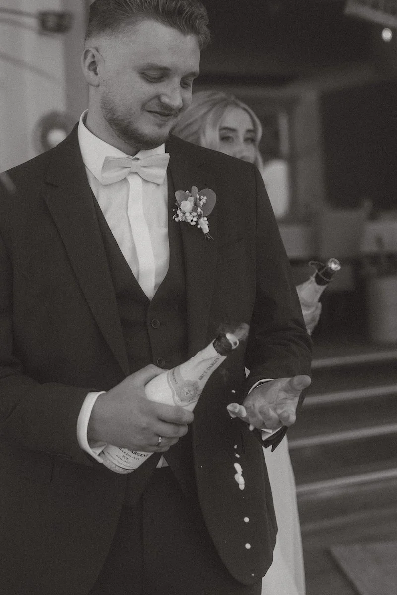 Der Bräutigam öffnet lachend die Sektflasche nach der freien Trauung bei Have’n’Hold am Herthasee in Holzappel, begleitet von einem Hochzeitsfotograf aus Darmstadt