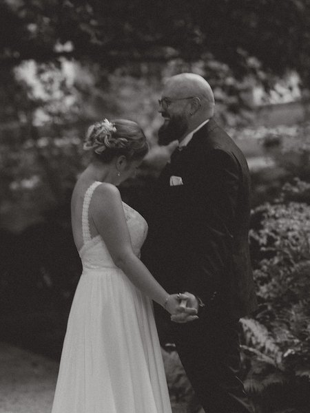 Ein Brautpaar hält Händchen bei einer Hochzeit im Andreasstift in Worms, im Hintergrund Bäume und Natur.