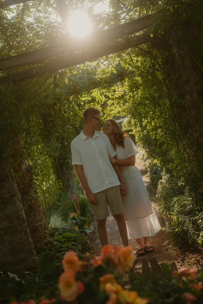 Ein Fotoshooting in Darmstadt zeigt ein verliebtes Paar bei einem Verlobungsshooting auf der Rosenhöhe in Darmstadt, innig lachend auf einem schmalen Gartenweg im warmen Abendlicht