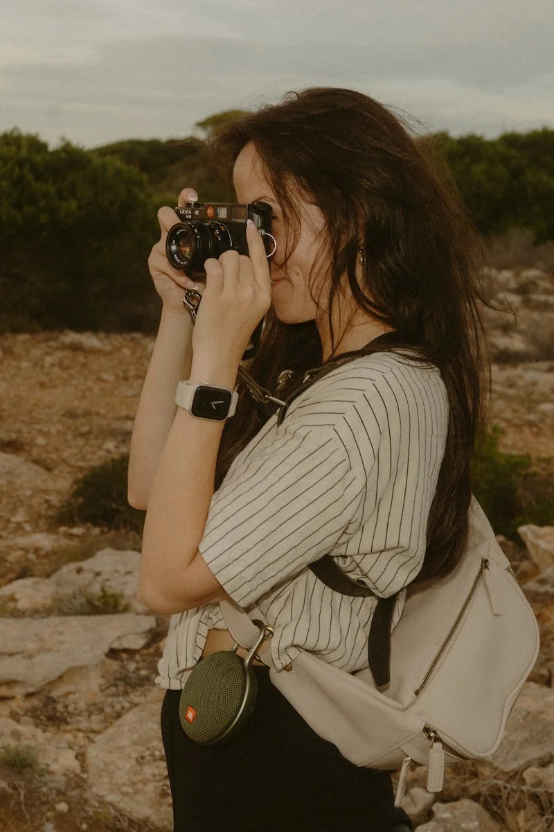 Eine Fotografin auf Mallorca mit analoger Kamera, konzentriert beim Fotografieren in natürlicher Umgebung ohne konkreten Anlass