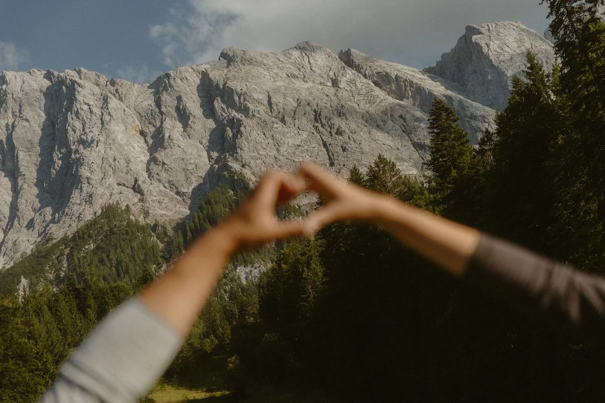 Ein Paar, dass zwei Hände in Form eines Herzes vor eine Bergkulisse in Südtirol hält