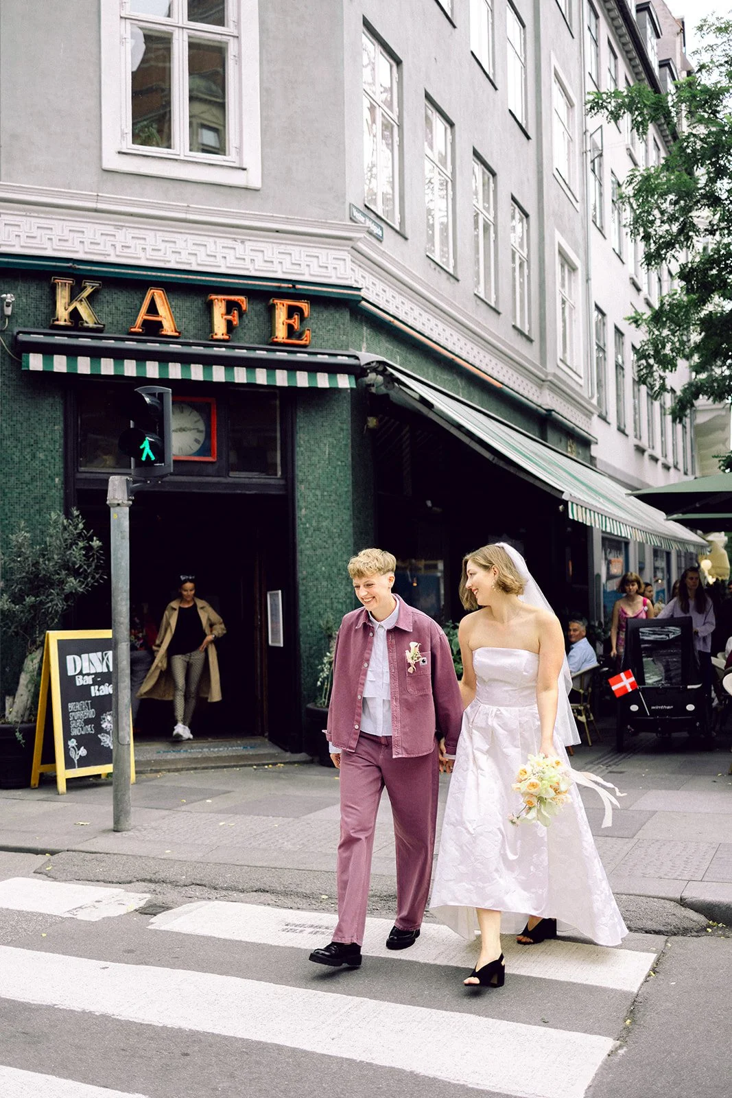 same sex couple walking hand in hand cross the street of copenhagen denmark with smiling faces in bride dress