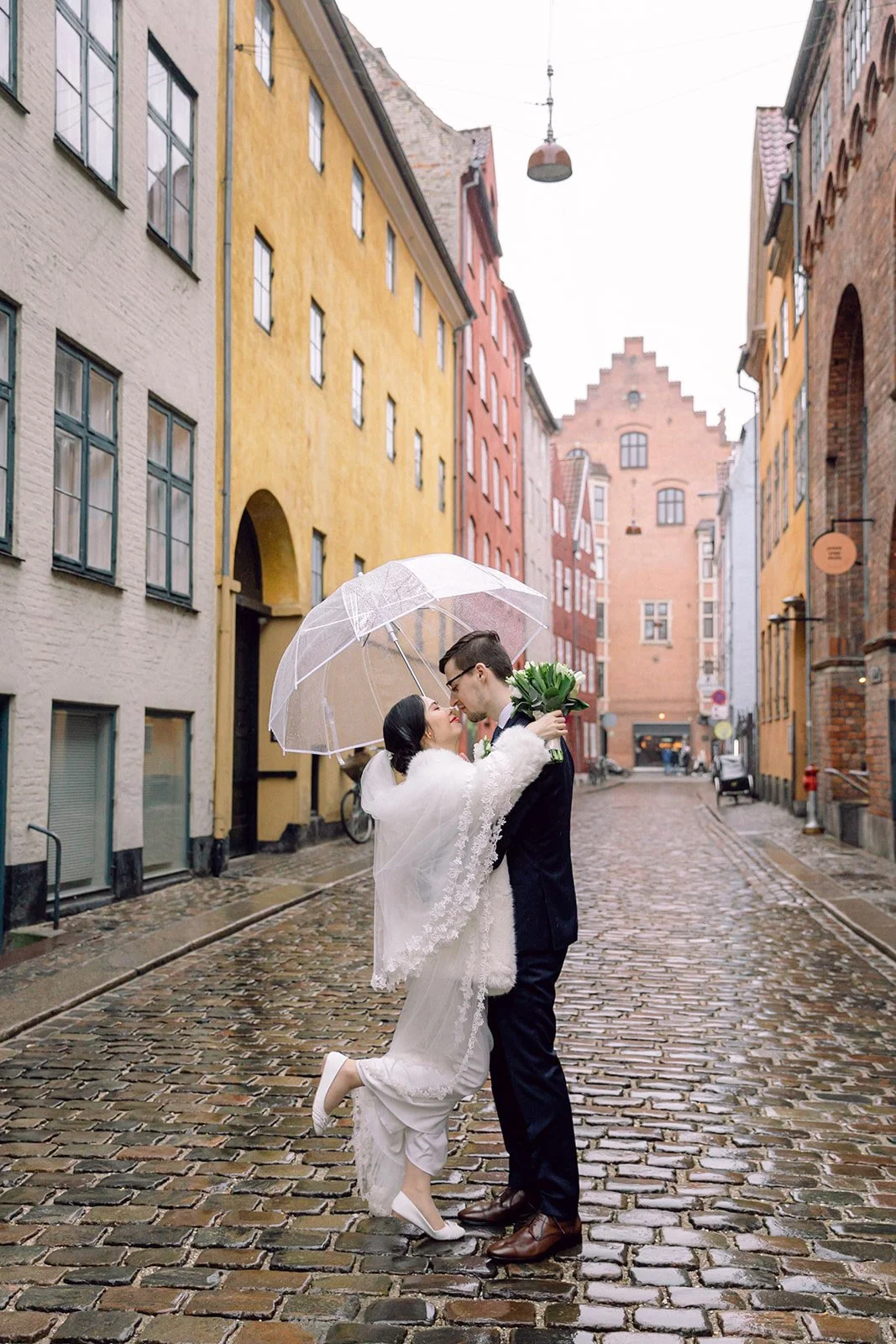 Couple kissing on Magstræde after getting married in Copenhagen denmark in a rainy day with transparent umbrella.jpg