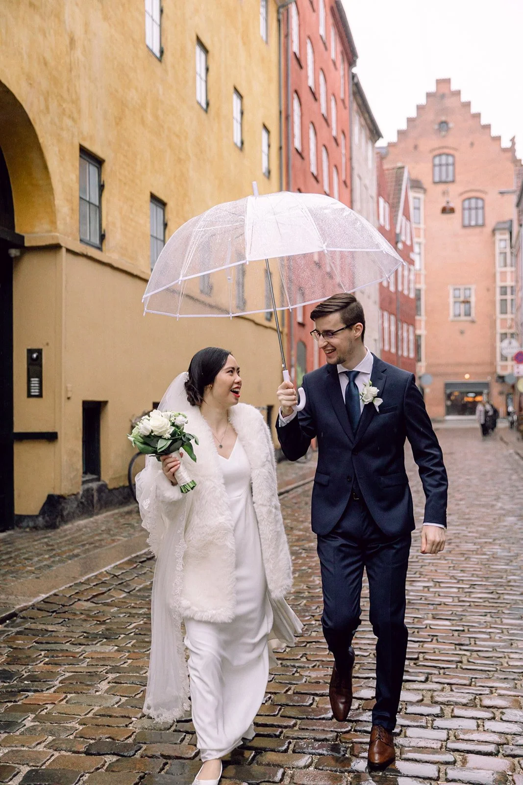 Couple walking on Magstræde after getting married in Copenhagen denmark in a rainy day with transparent umbrella.jpg