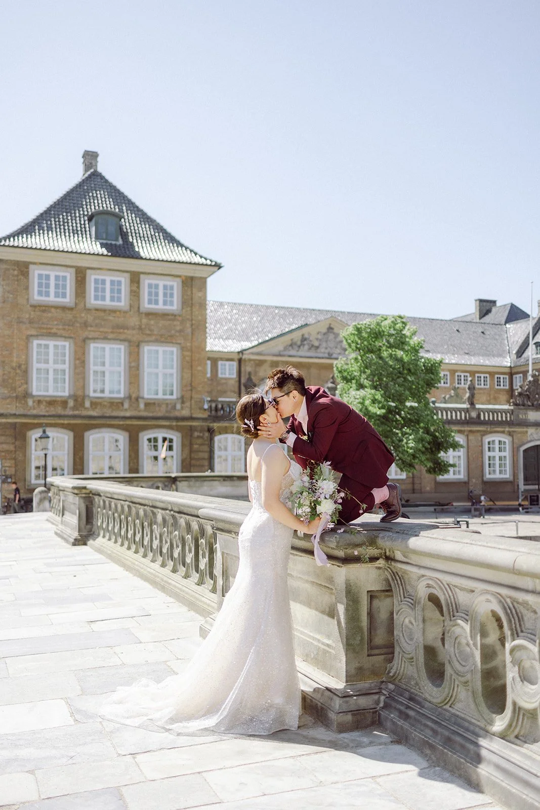 same sex Couple kissing in christiansborg slot marble bridge sunny day after getting married in copenhagen city hall with fine art style bouuquet film inspired.jpg