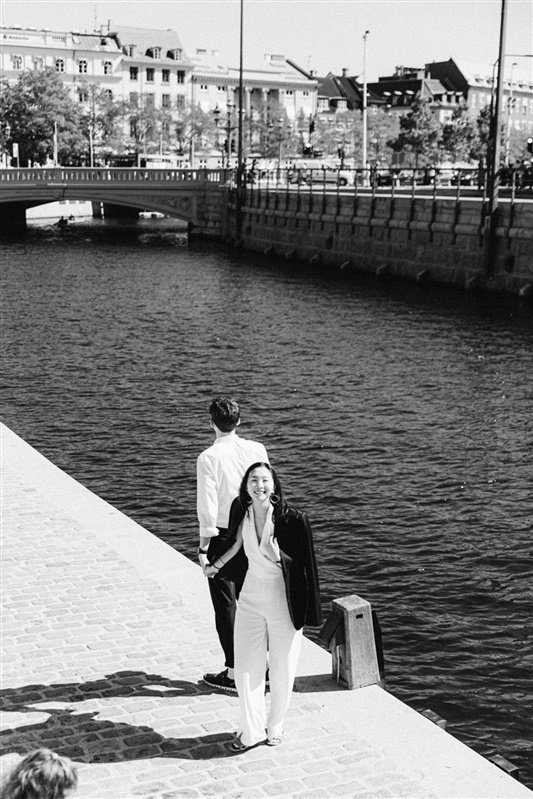 Bride and groom walking by canal in copenhagen denmark bride in white suit black and white bride smiling to the camera.jpg