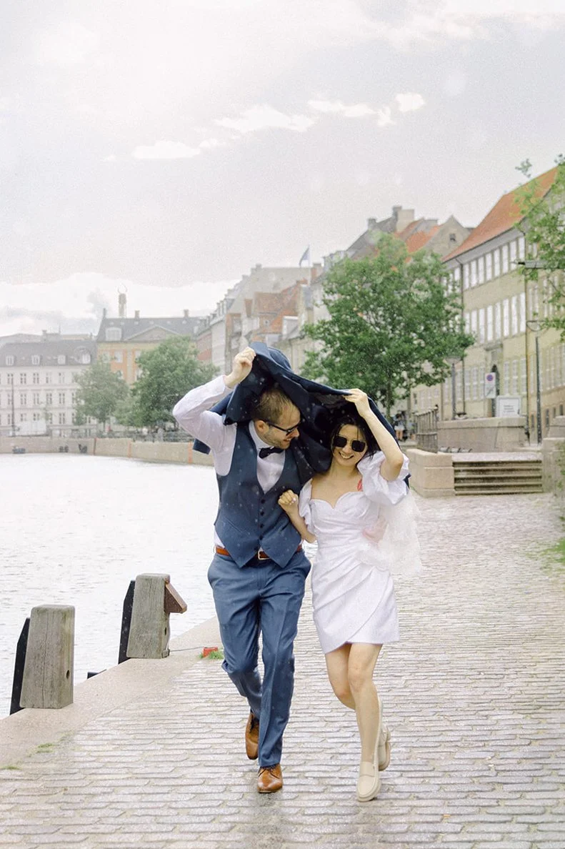 Couple running in the rain with jacket cover over the head laughing after getting married in copenhagen.jpg