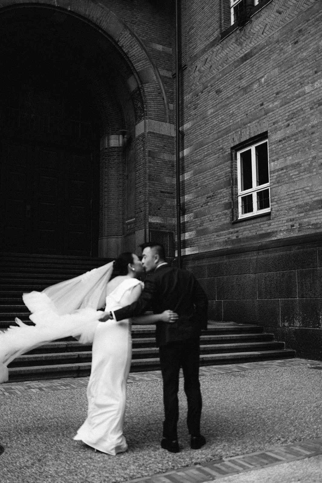 Couple walking in copenhagen city hall garden after getting married in denmark veil flying away black and white.jpg