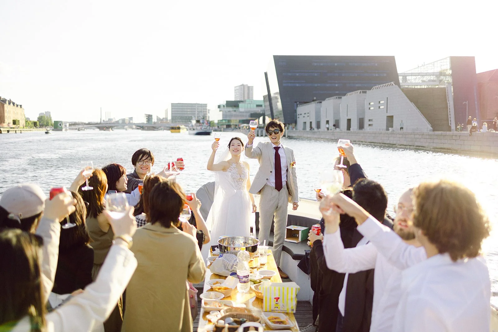 summer afternoon a chinese couple toasting with guests on a boat in copenhagen canal after getting married in denmark with Hey Captain