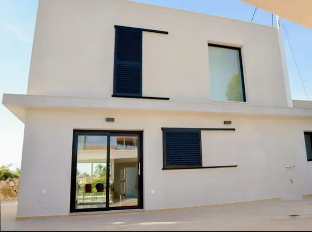 Modern two-story house with white exterior, large windows, and black shutters, with a patio area in front.