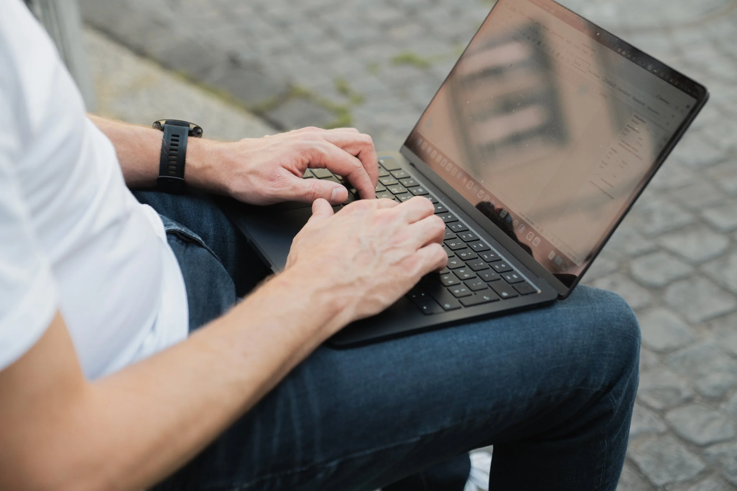Hände tippen auf einem Laptop im Freien – Online Coaching funktioniert überall, auch unterwegs.