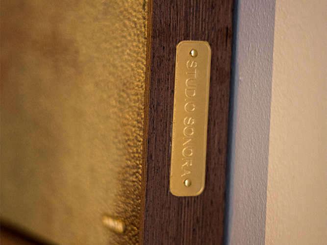 Close-up of a brass nameplate with the text 'SOUKOS S.P.ALL' mounted on a wooden surface.