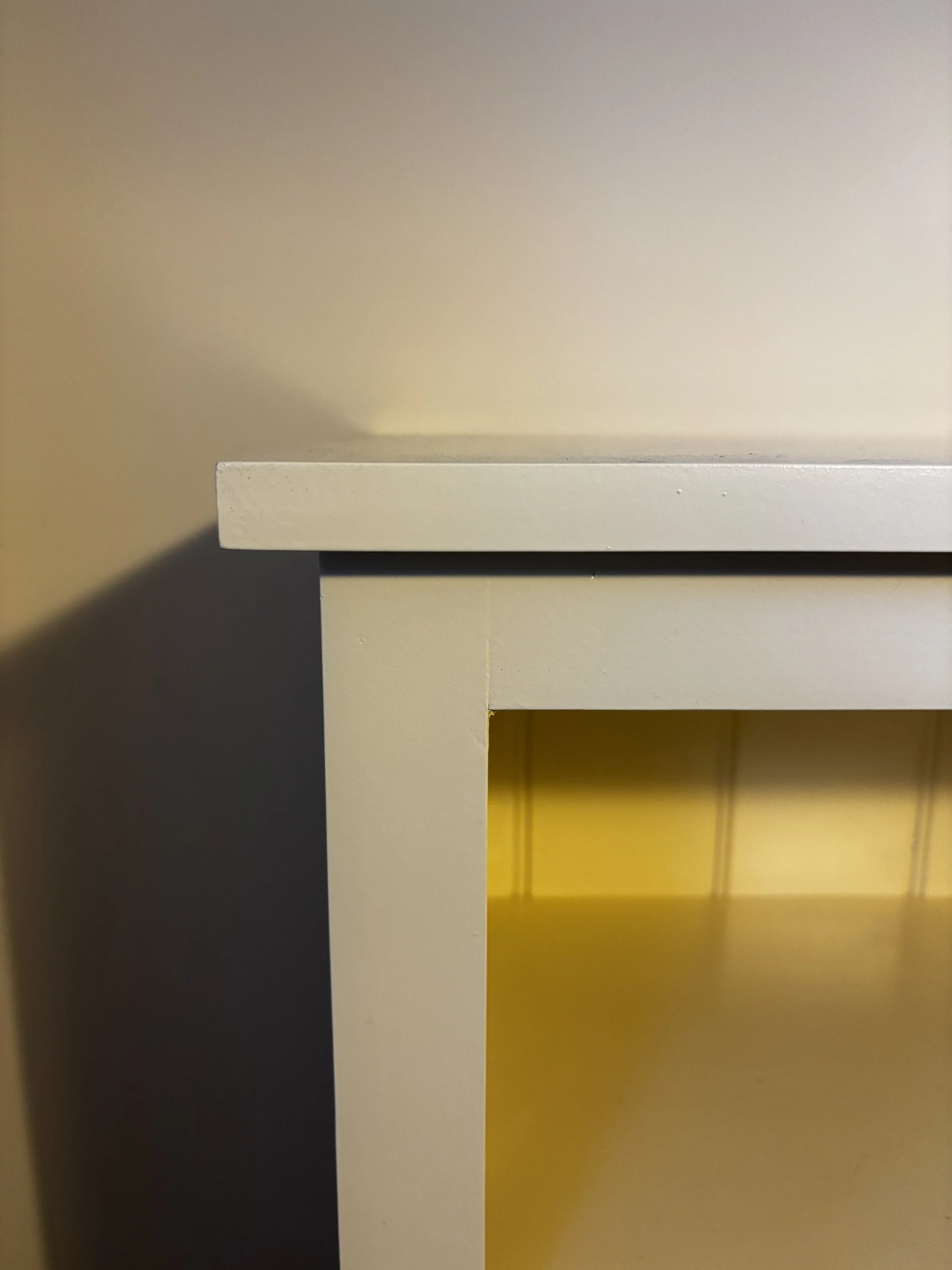 Close-up of a white piece of furniture, possibly a drawer or cabinet, with a shadow cast on the wall behind it.
