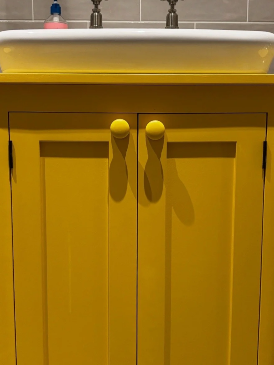 Yellow cabinet under a bathroom sink with two doors and round yellow knobs.