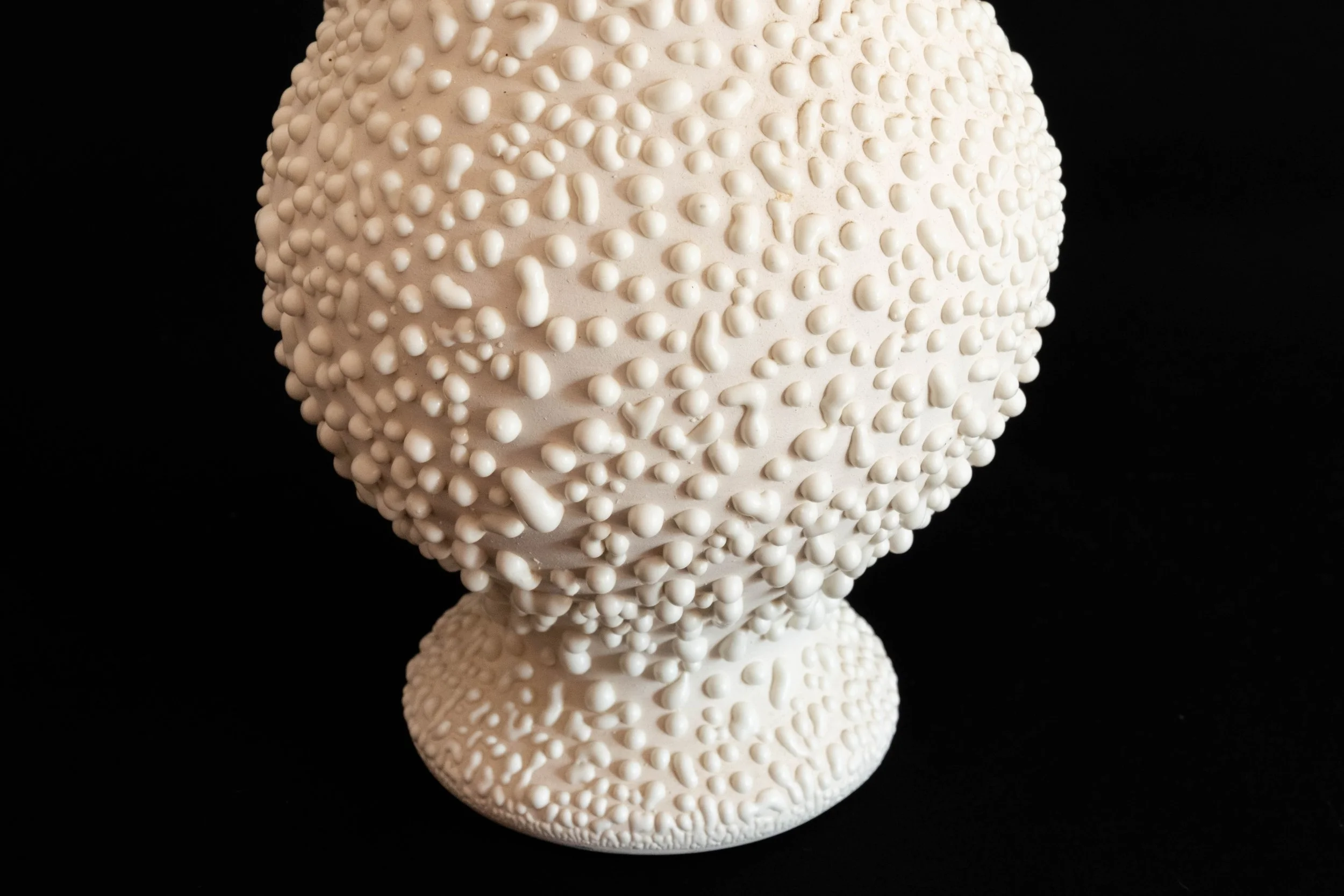 A white ceramic decorative vase with a textured surface of small raised bumps, set against a black background.