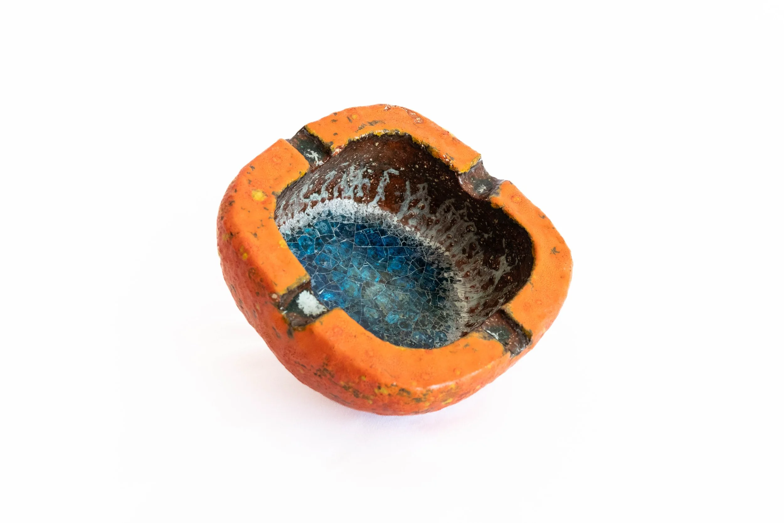A broken orange ceramic object with blue and white cracked glaze interior, resembling a small bowl or cup, on a white background.
