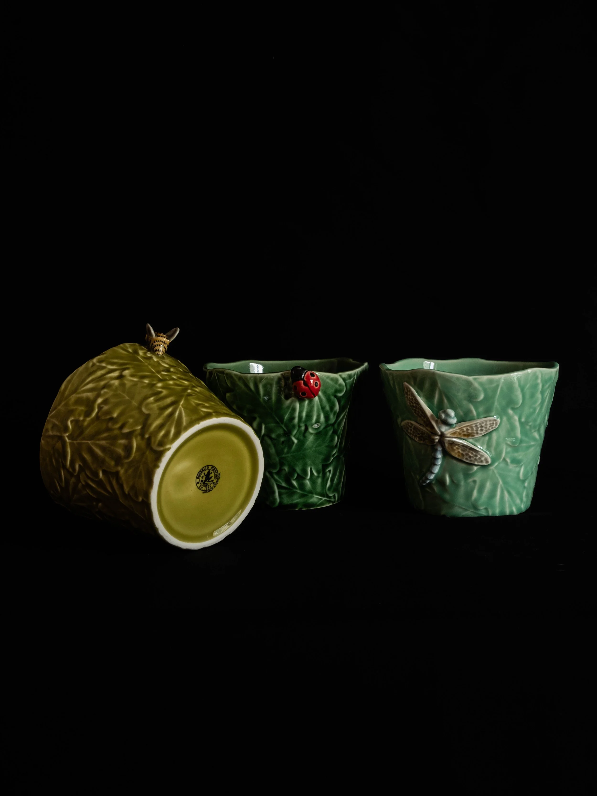 Three ceramic plant pot mugs with insect decorations, two green and one yellow, on a black background.