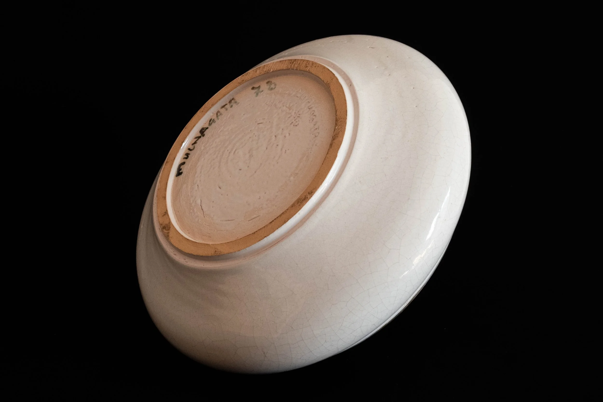 Upside-down white ceramic bowl showing the bottom with markings and a crackle glaze pattern.