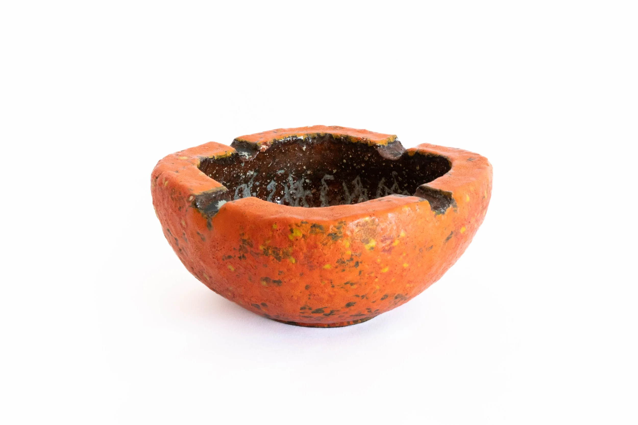 A ceramic bowl shaped like a pumpkin with a hollow interior, orange exterior, and black accents around the rim, set against a plain white background.