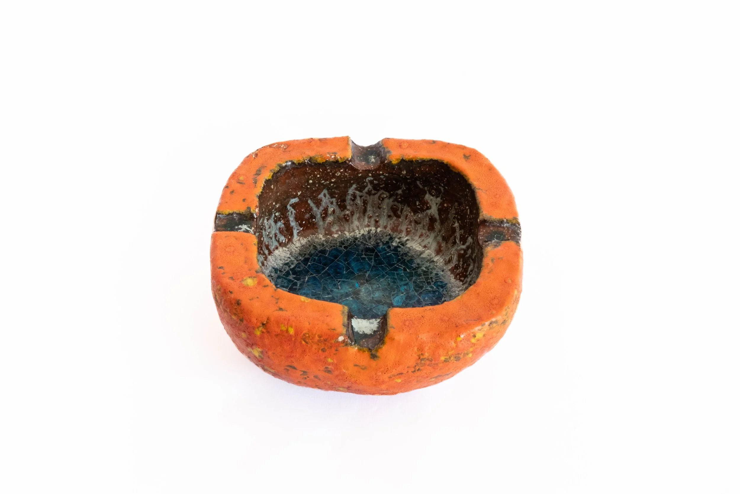 A broken orange ceramic ashtray with black and blue interior on a white background.