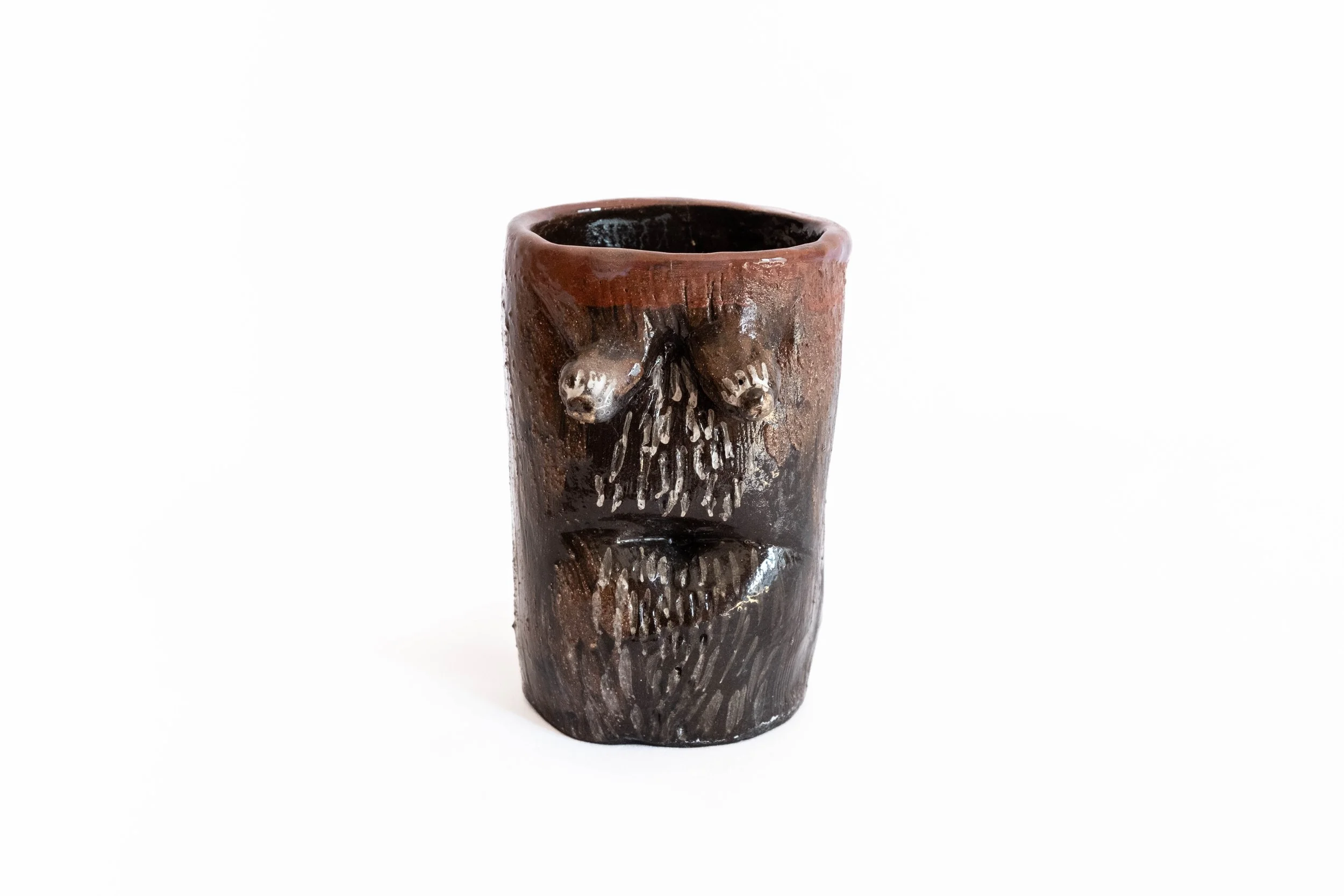 A brown ceramic mug with carved and painted details of a bear's face and fur texture.