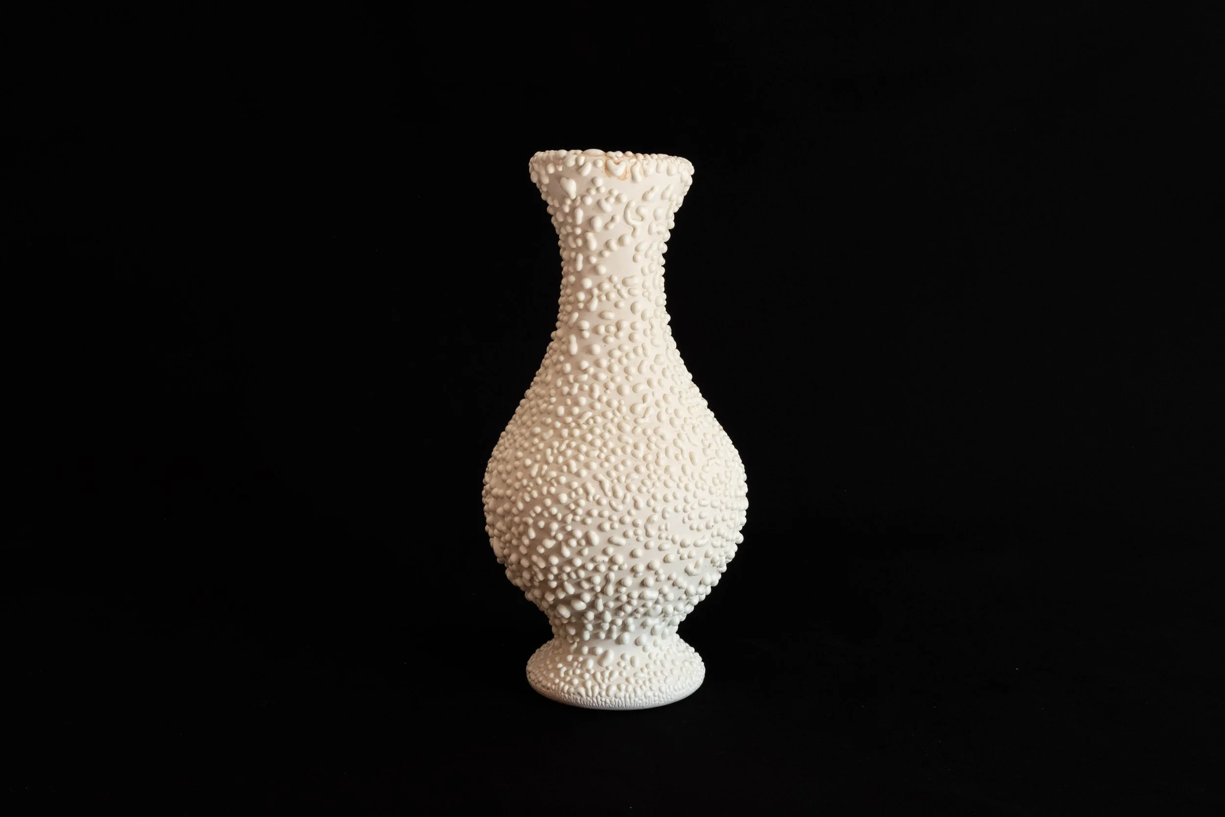 A white vase with a textured surface made of small, round bumps, set against a black background.