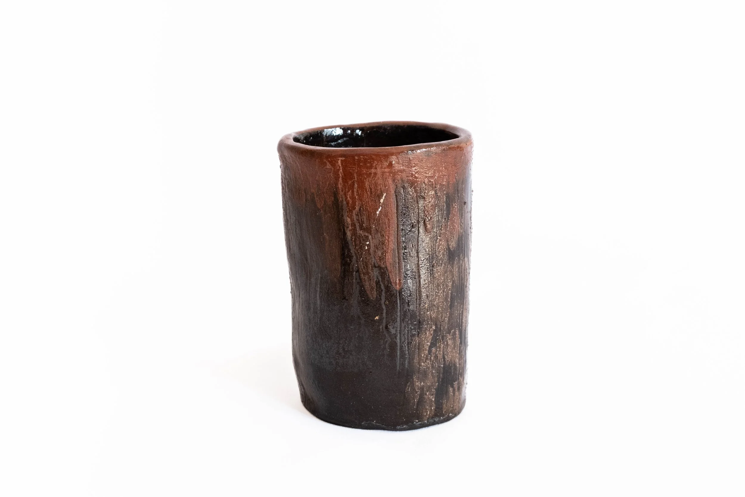 A tall, weathered ceramic vase with a dark brown and reddish surface, standing against a white background
