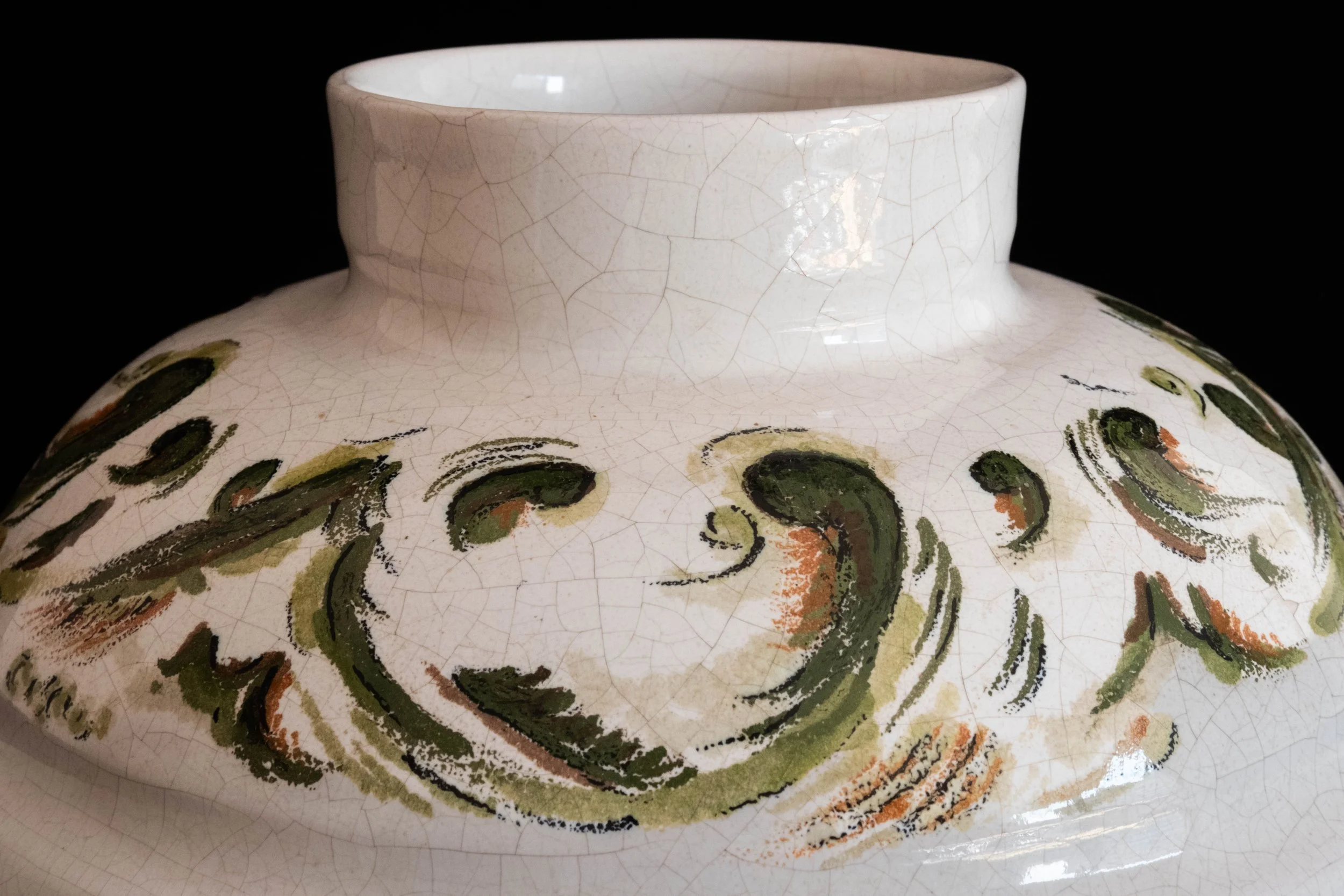 Close-up of a ceramic vase with a cracked glaze finish, decorated with green, orange, and black abstract swirling patterns.