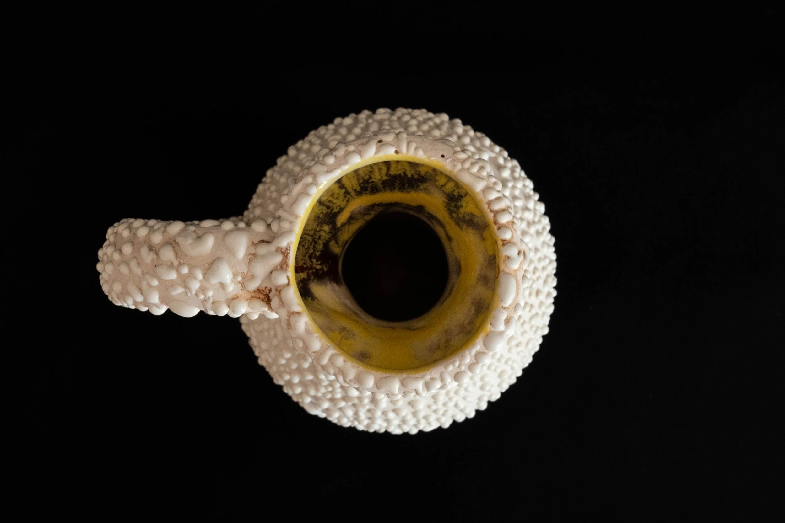 Top view of a beige beaded ceramic mug with a yellow and black interior, placed on a black background.