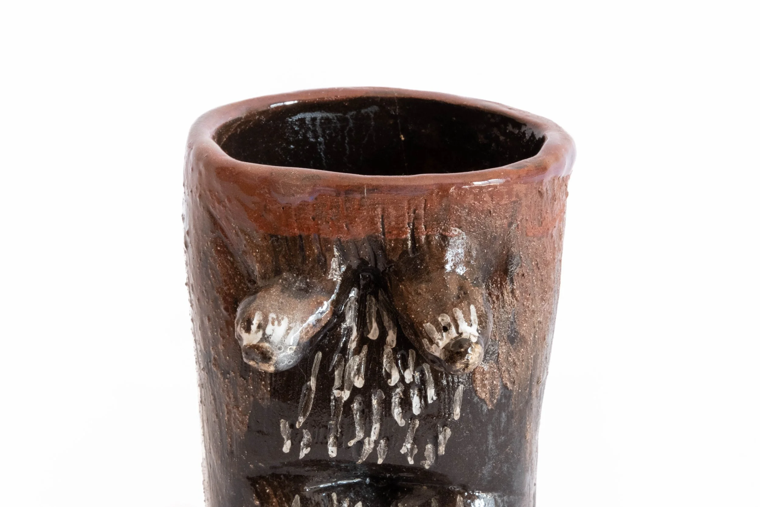 Close-up of a rustic ceramic mug with textured surface and decorative animal heads with long beards attached to the front, featuring a dark interior.