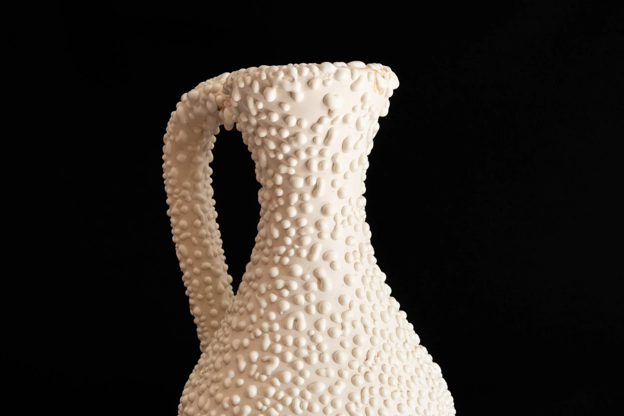 Close-up of a textured white ceramic pitcher against a black background.