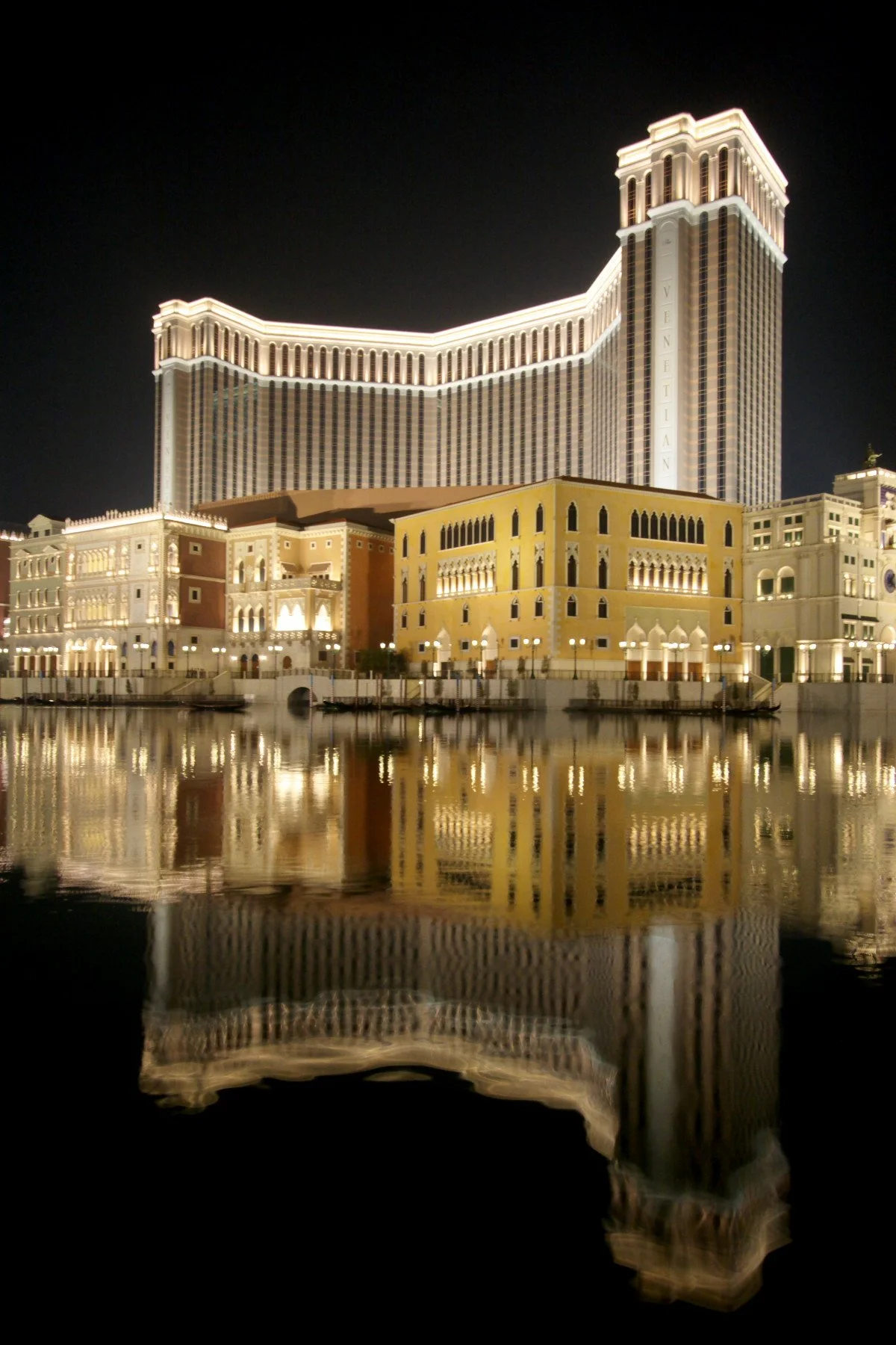 Night view of The Venetian hotel and casino in Macau with reflected lights on water.