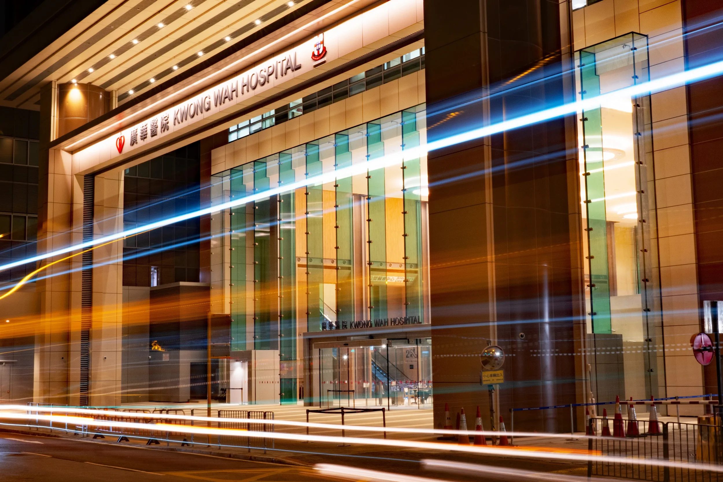 Exterior of Kwong Wah Hospital at night with light trails from moving vehicles.
