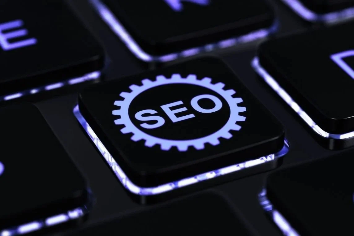 A close-up of a computer keyboard key labeled 'SEO' with a gear symbol, illuminated by purple backlighting.